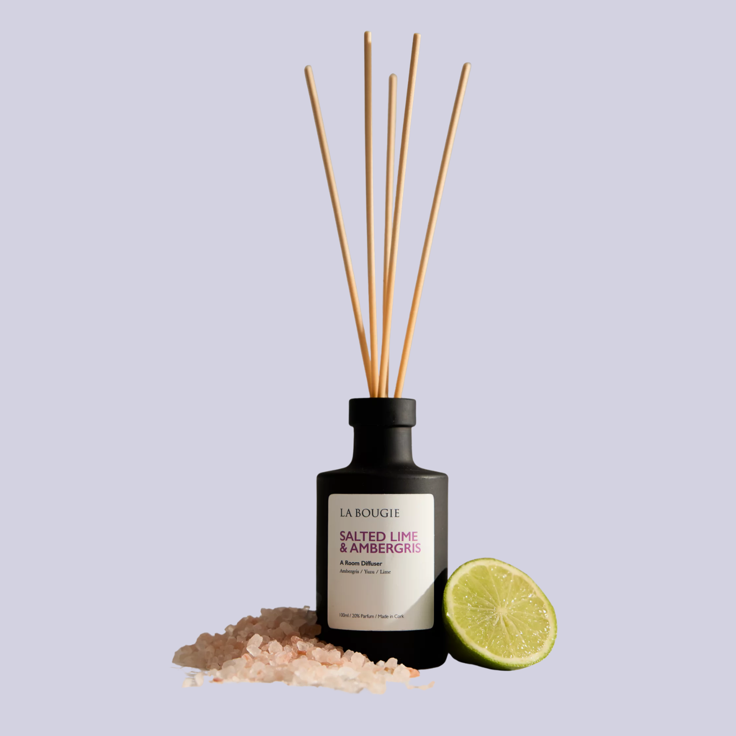 A black reed diffuser beside a heap of ambergris and a sliced lime