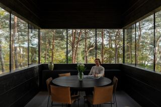 man sat at round table surrounded by glazing and trees at Villa Nikkesmelle by Gartnerfuglen