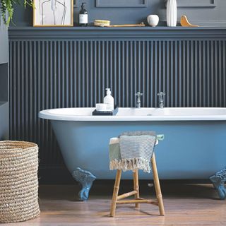 Blue bathroom with blue panelling and a lighter blue bathtub, and a woven basket standing next to it