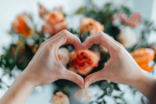 A bunch of roses with a person making a heart-shape with their hands in front.