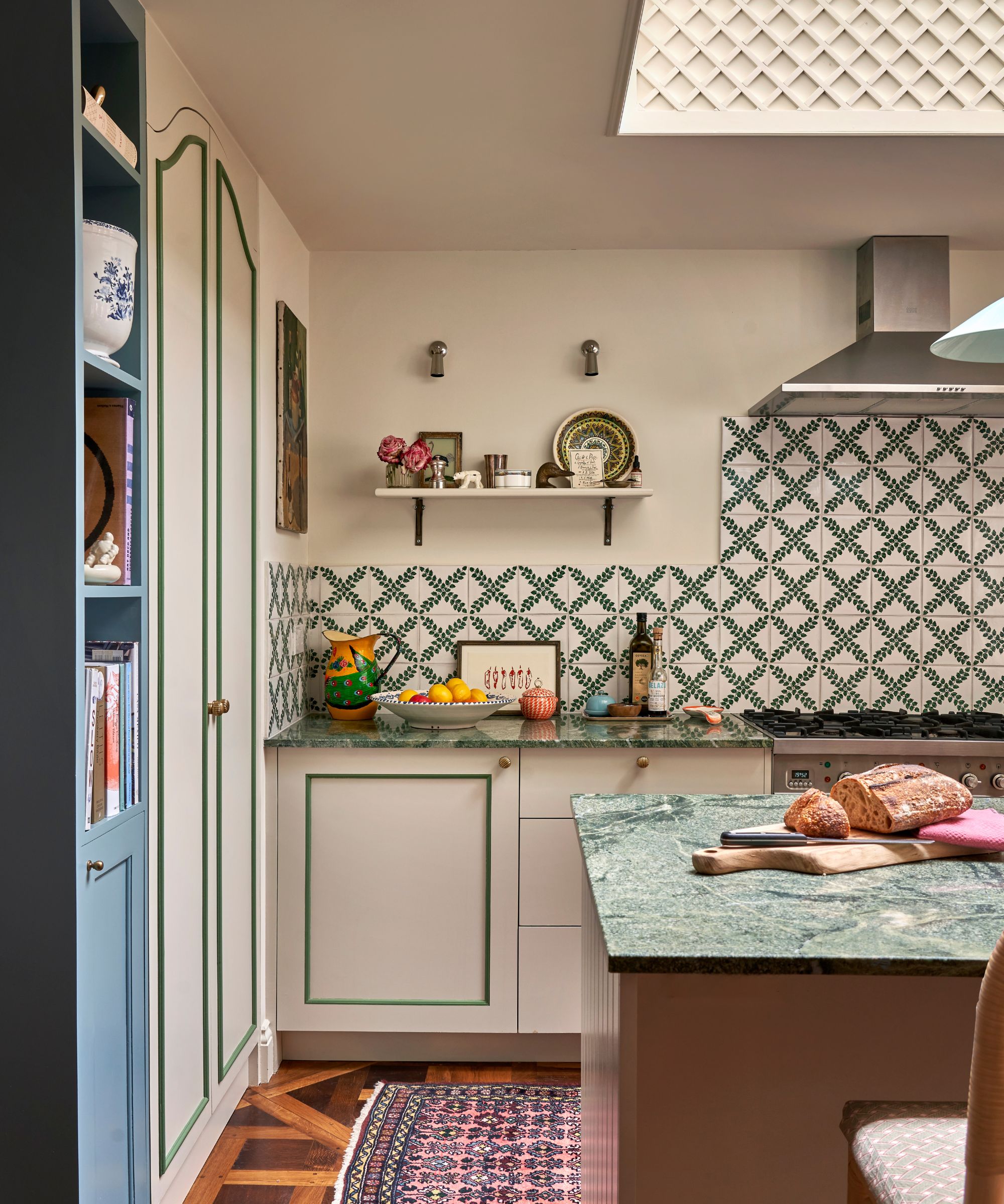 A kitchen with neutral walls and cabinets, white and green patterned wall tiles, and green stone countertops
