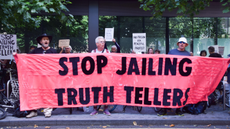 Protesters stand outside Soutwark Crown court holding a large red banner that says 'stop jailing truth tellers'