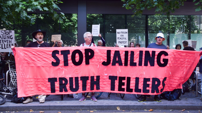 Protesters stand outside Soutwark Crown court holding a large red banner that says &#039;stop jailing truth tellers&#039;