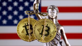Two bitcoins held by Lady Justice in front of a US flag