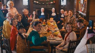 The cast of Call the Midwife sit around a table, smiling at a camera, in the 2023 Christmas special