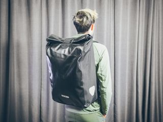 Will Jones, wearing the Ortlieb Messenger, one of the best backpacks for cycling, stands in front of a wall
