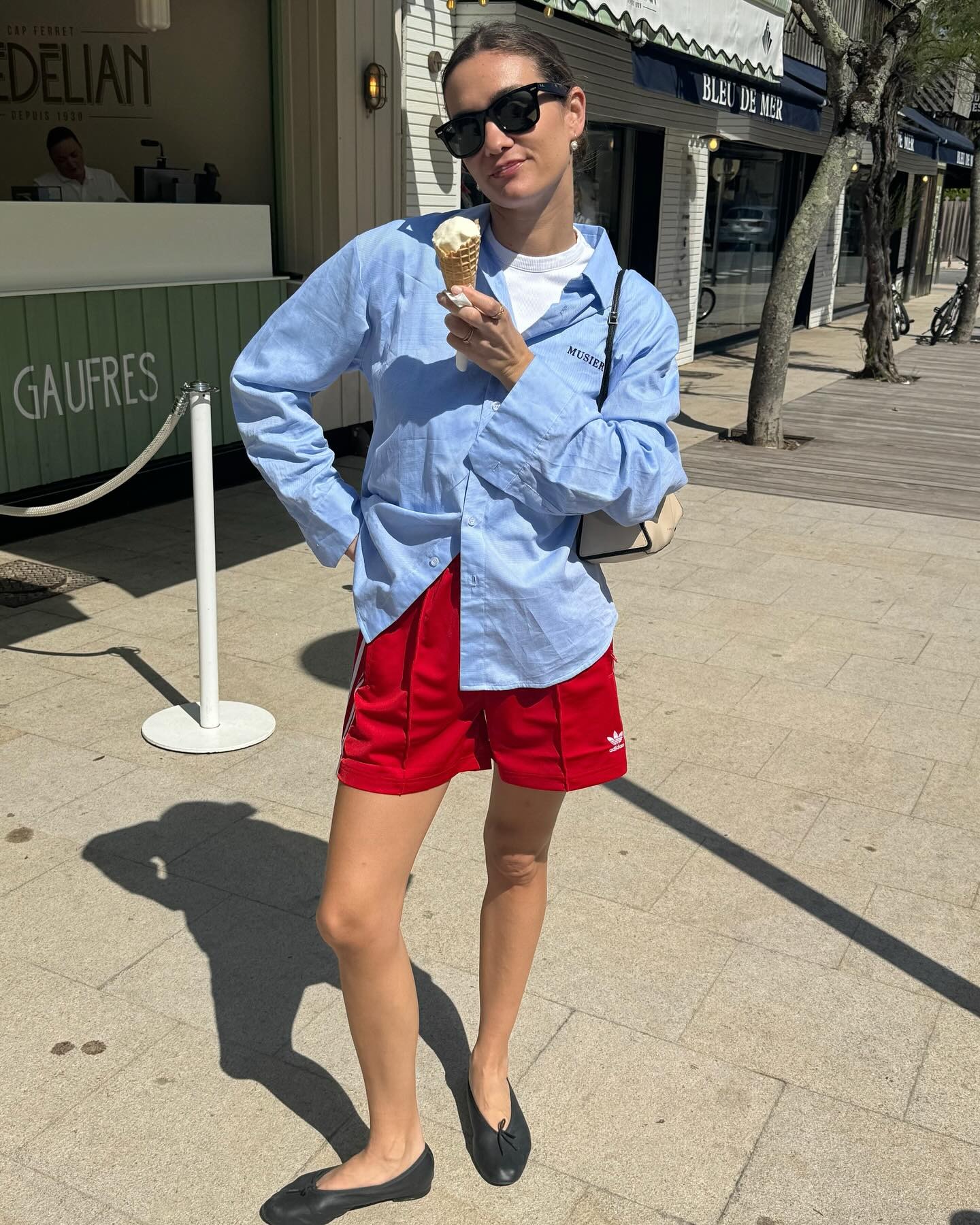 Influencer @annelauremais poses for a photo with an icecream wearing red sports shorts with a shirt and black ballet flats.