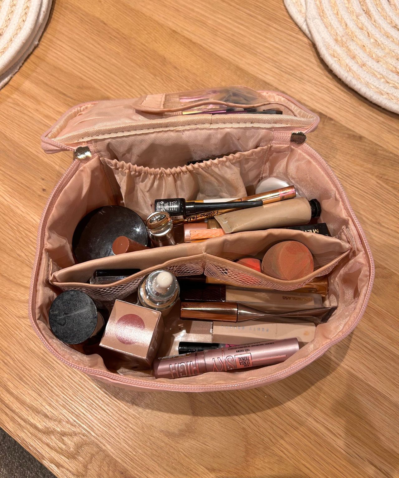 Pink makeup bag with lots of products in on a table