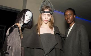 Left, model is seen wearing white face paint with a satin bomber jacket. Middle model wears a triangular crown and oversized wool coat. Right, model wears a tailored patchwork coat.