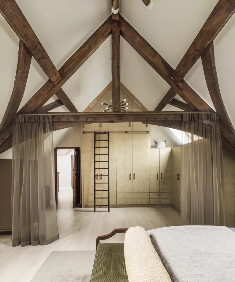 A bedroom with a beamed, vaulted ceiling and tall cabinetry with a ladder