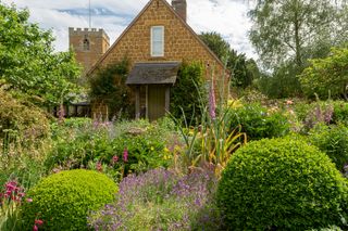 Side view of cottage with densely planted borders full of flowers