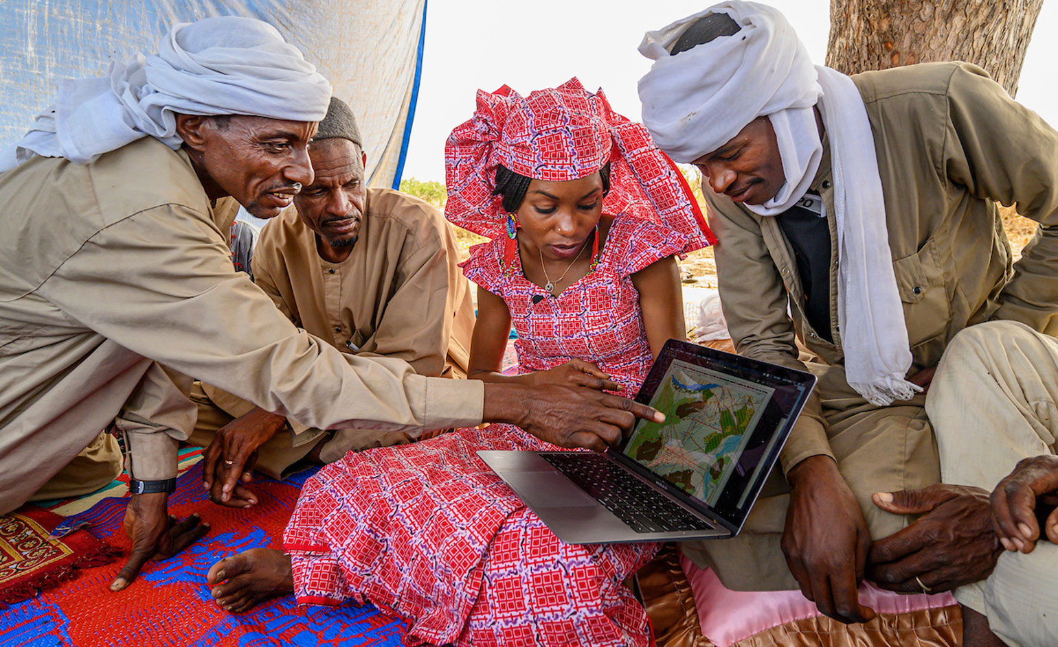 Woman holding a computer surrounded by people pointing at it