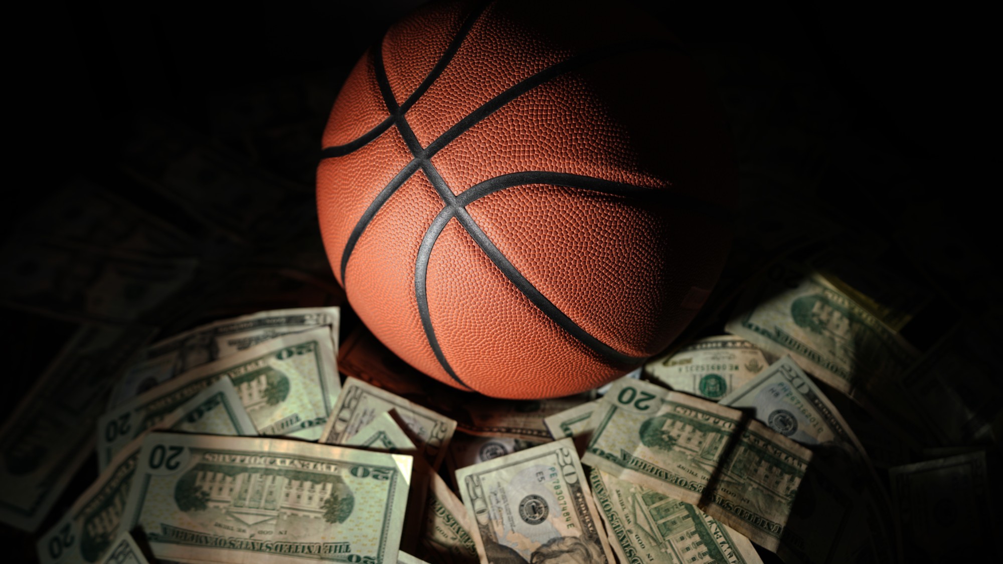 A basketball on a pile of money on dark background
