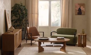 Green sofa, tan leather chair, oval wooden coffee table and sideboard in warm, earthy mid-century room.