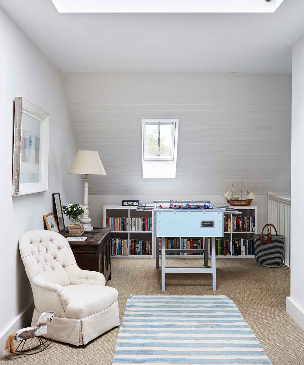 A neutral playroom with cream armchair, low bookshelves, a pale blue striped rug and table football.