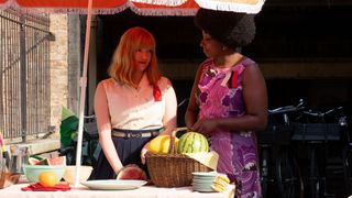 Rosalind and Joyce standing under a sun shade talking and chopping fruit