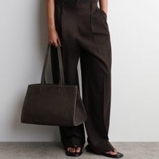 A COS model wearing brown trousers, sandals, and a brown suede tote bag.
