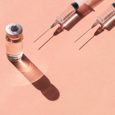 Pattern made with many plastic disposable sterile syringe and sealed vial of liquid remedy placed on pastel peach orange background with shadows and light reflections