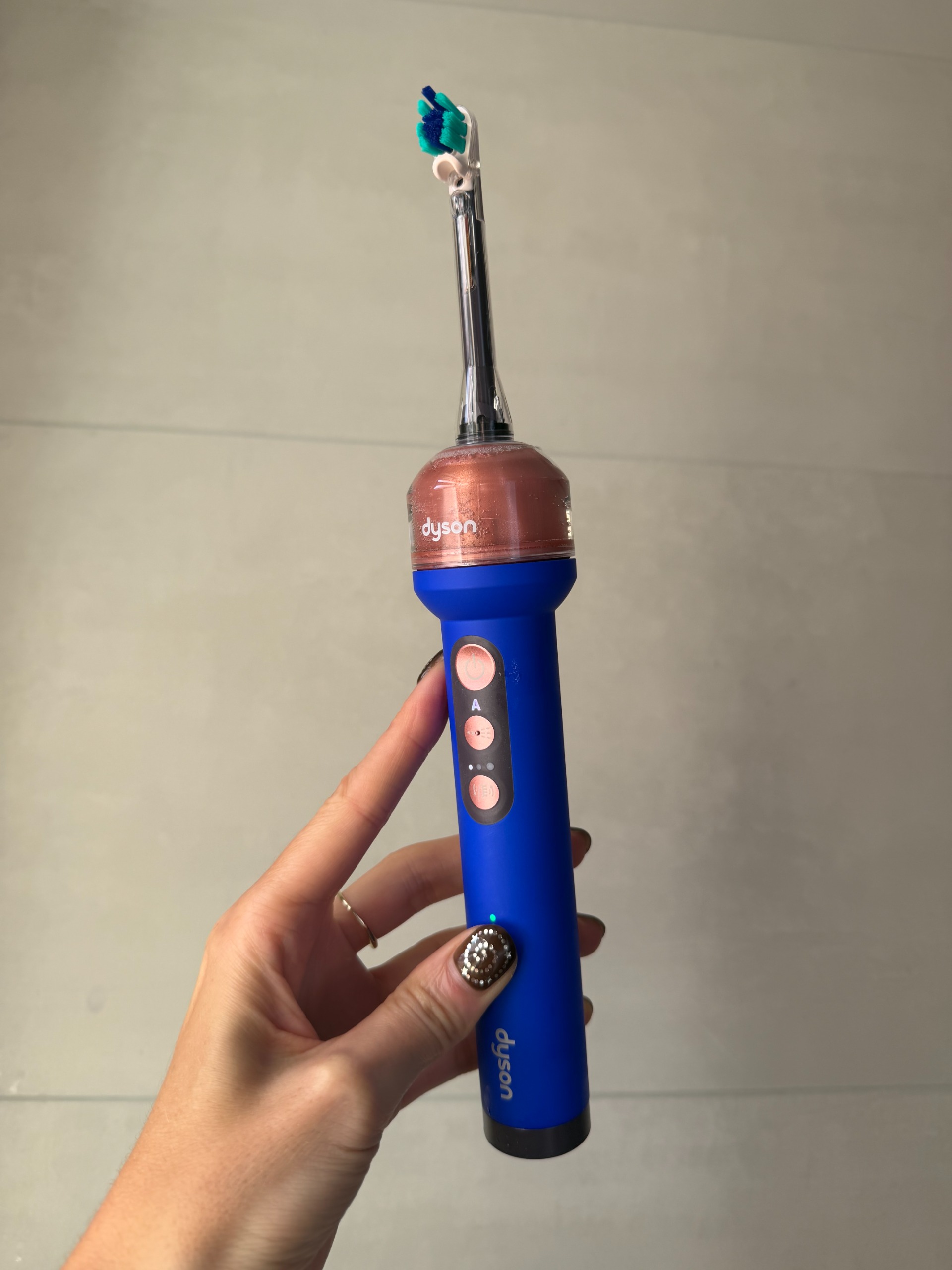 a close up of a hand holding a blue Dyson Camera Jet toothbrush