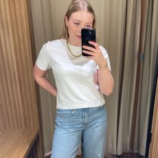 Woman wears white T-shirt, blue jeans and gold necklace