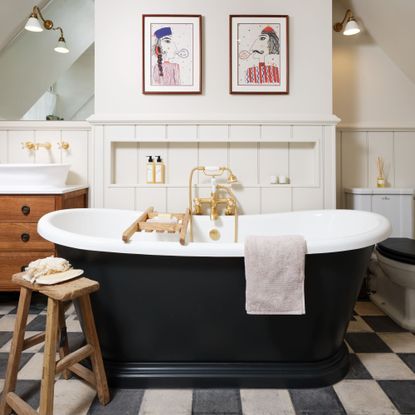 freestanding bath on white and black tiles in front of white paneled wall with artwork