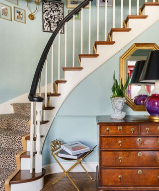 light blue stairwell with antique wood dresser, gold mirror, and leopard print stairrunner