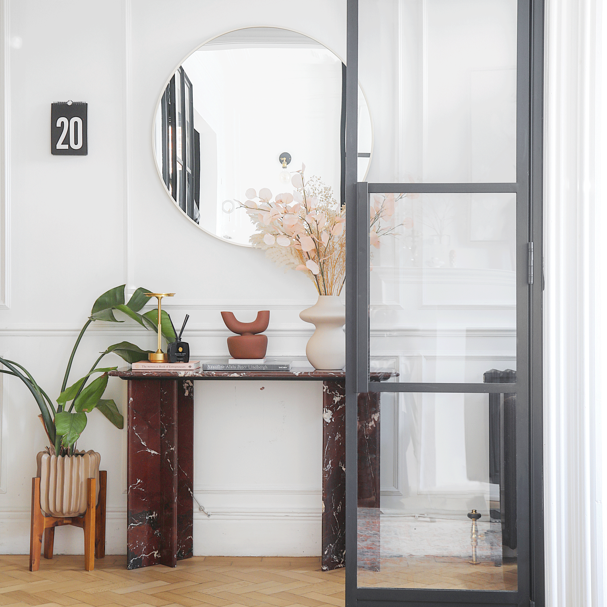a hallway with a marble console table and large frameless round mirror beside an internal glazed door