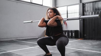 A woman performing barbell front squat in a gym