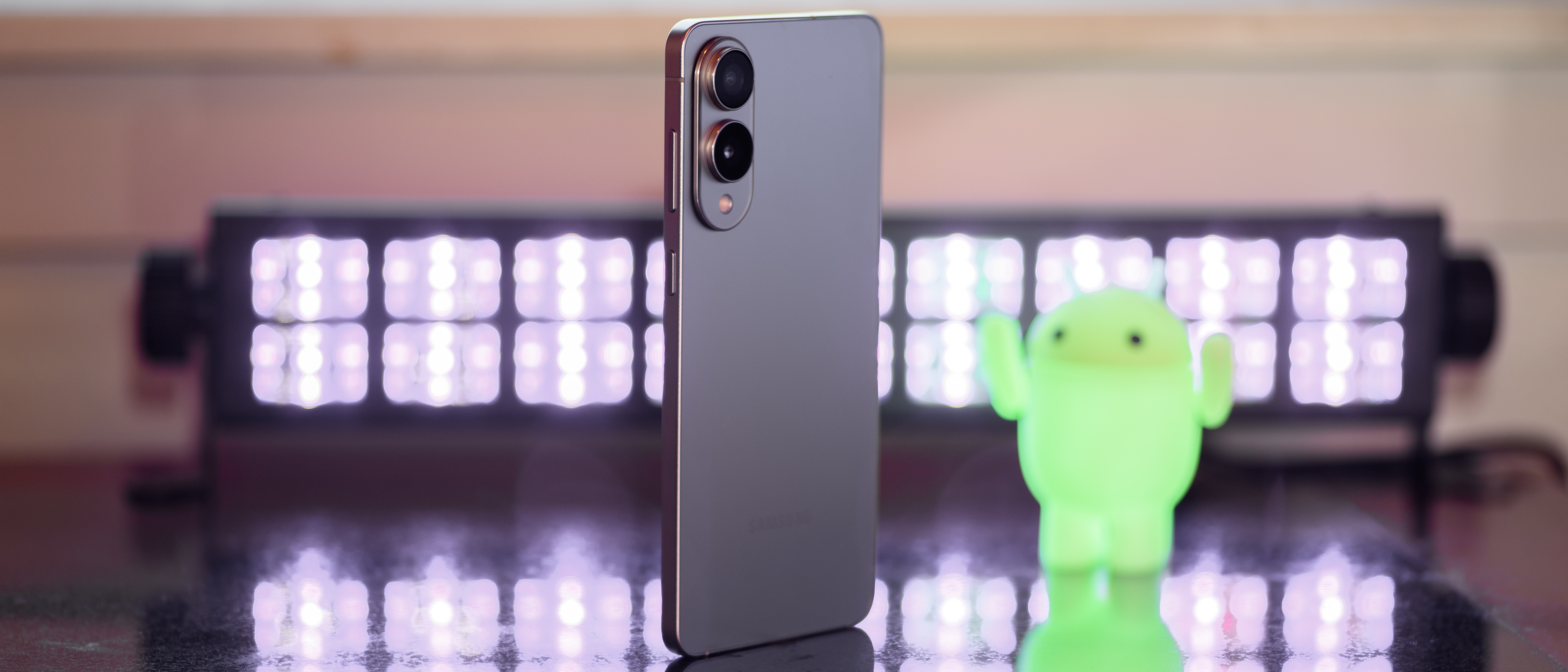 Samsung Galaxy S25 Edge from a 3/4 angle with black lights and an Android figuring blurred in the background