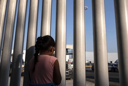 Girl looking through fence at U.S. Mexico border.