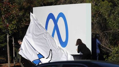 A woman changes Facebook's sign from the "like" icon to the new Meta company logo