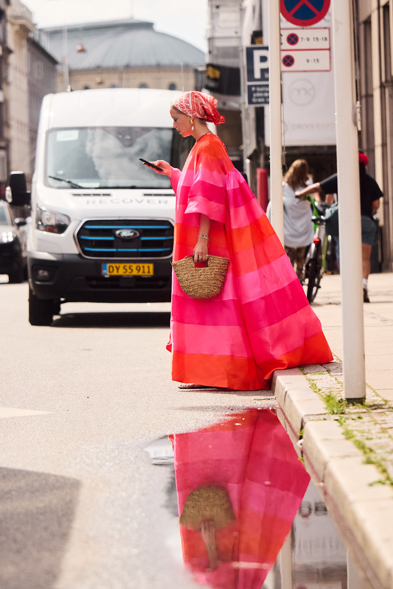 a woman wearing a pink and orange striped dress in a bandana and straw bag
