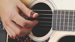 A man plays acoustic guitar with a thumb pick