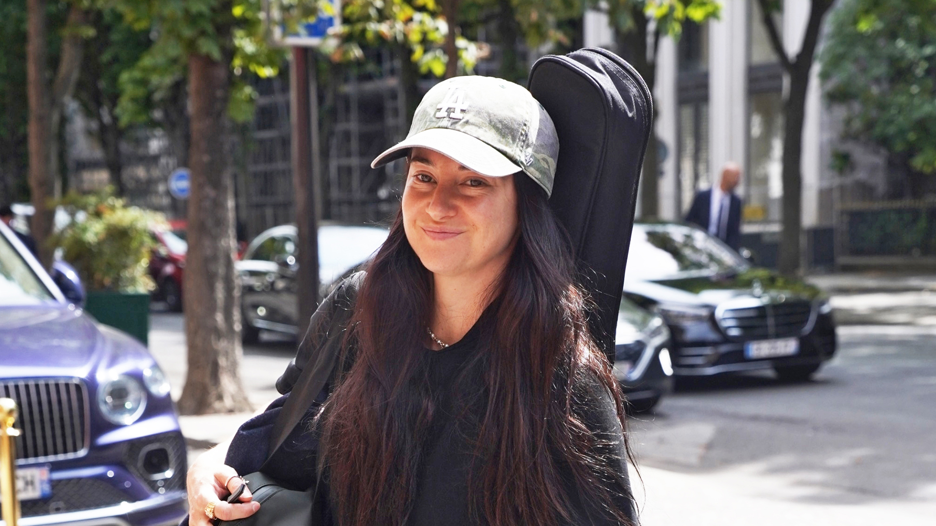 Shailene Woodley wearing a green baseball cap, black t-shirt, olive pants, and black loafers.