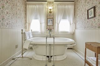 A white bathtub in the middle of a cozy wallpapered bathroom at the Red Lion Inn in Massachusetts with light coming in through the windows