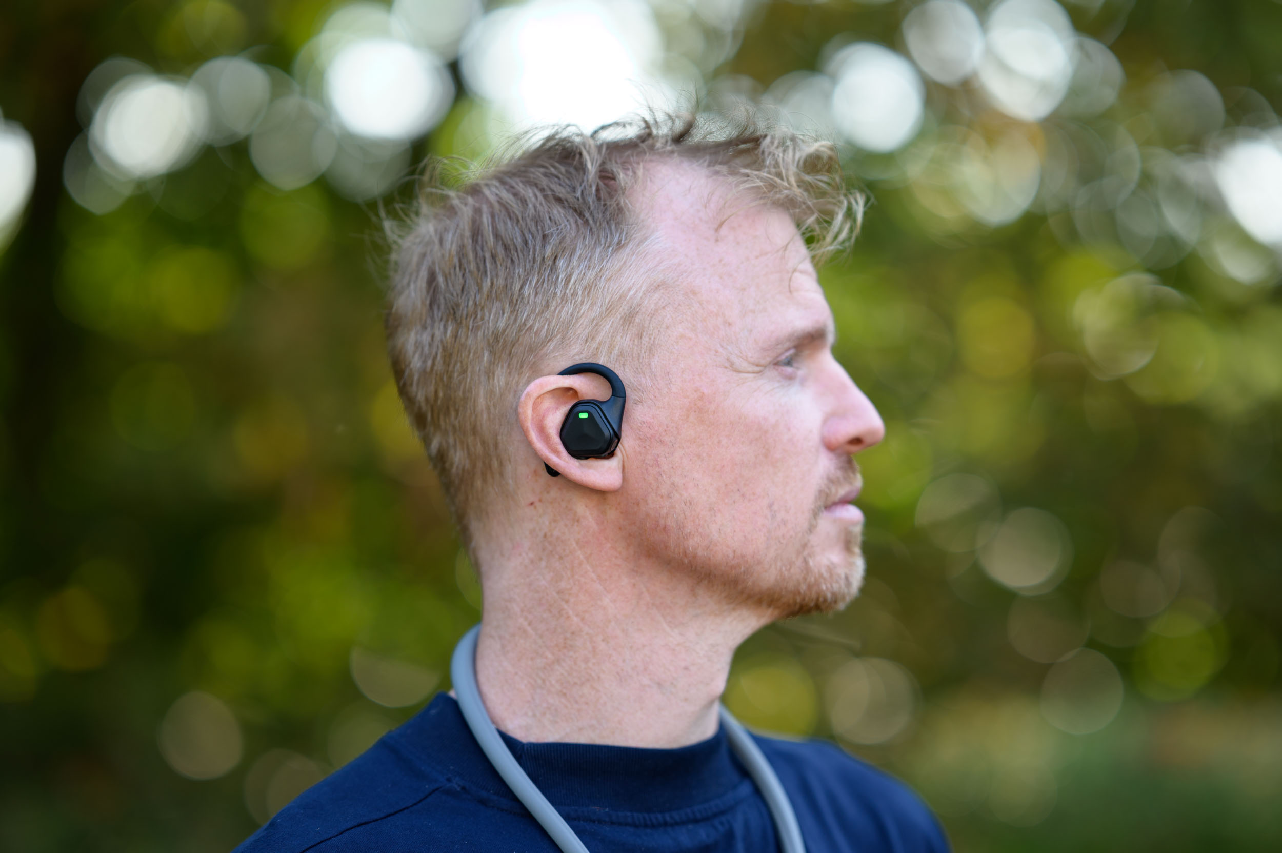 Closeup of the Insta360 POV Head Tracker accessory in Tim Coleman's ear, outdoors with dappled light in background foliage