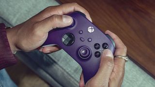 Xbox wireless controller in Astral Purple being gripped by a pair of hands and used to play a game.