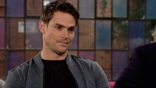 Mark Grossman as Adam Newman sitting at a table outside in The Young & The Restless