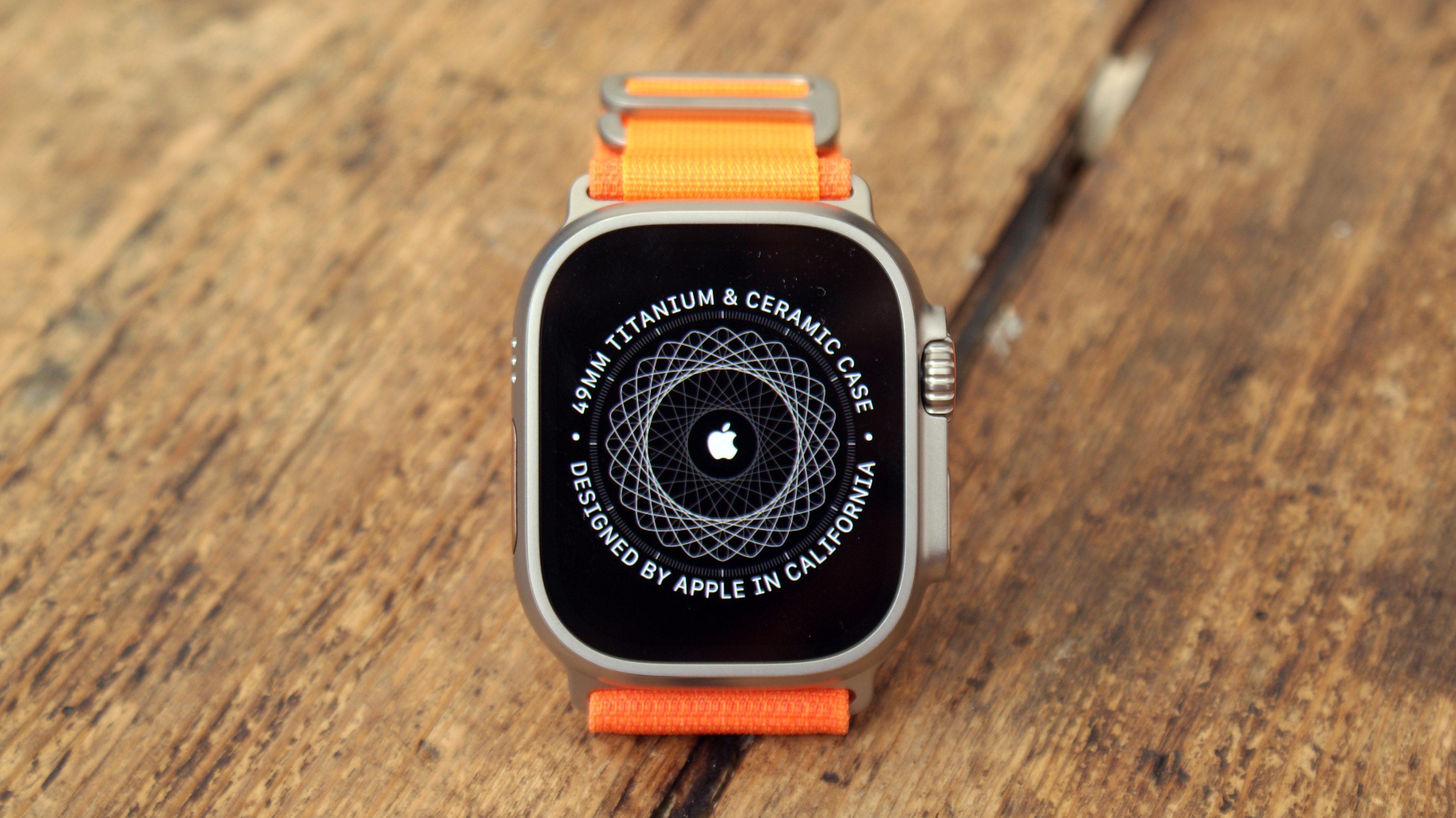 Apple Watch Ultra with orange strap pictured on a wooden table
