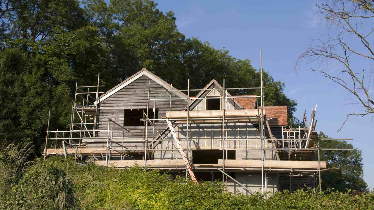 A new home, shot from below, under construction. The house is surrounded by scaffolding and is being clad in timber. The property sits in a wooded area.