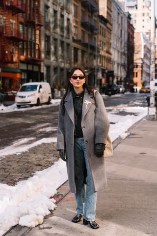 Emma Childs wearing a gra coat, black sweater, jeans, and black boots