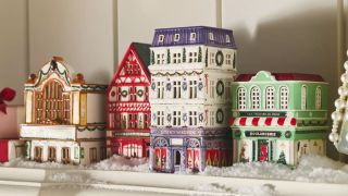 Four colorful ceramic Christmas houses sit on top of a mantelpiece in amongst fake snow and pearl decorations