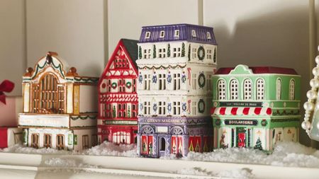 Four colorful ceramic Christmas houses sit on top of a mantelpiece in amongst fake snow and pearl decorations