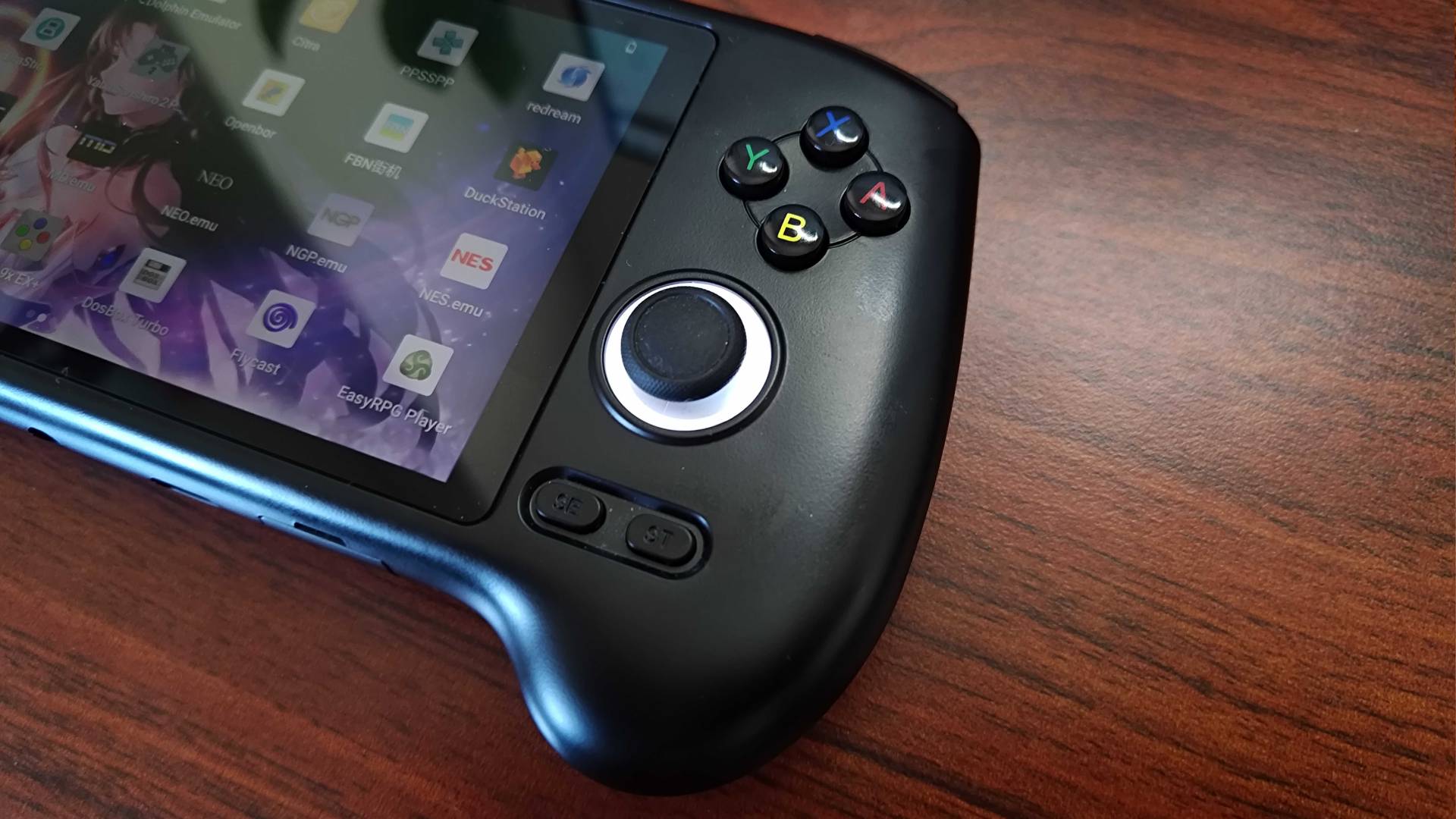 Close up of Anbernic RG556 thumbstick and buttons with handheld sitting on woodgrain desk.