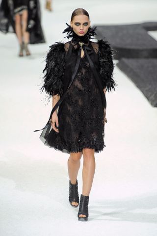 a model wears a feathery black Chanel dress