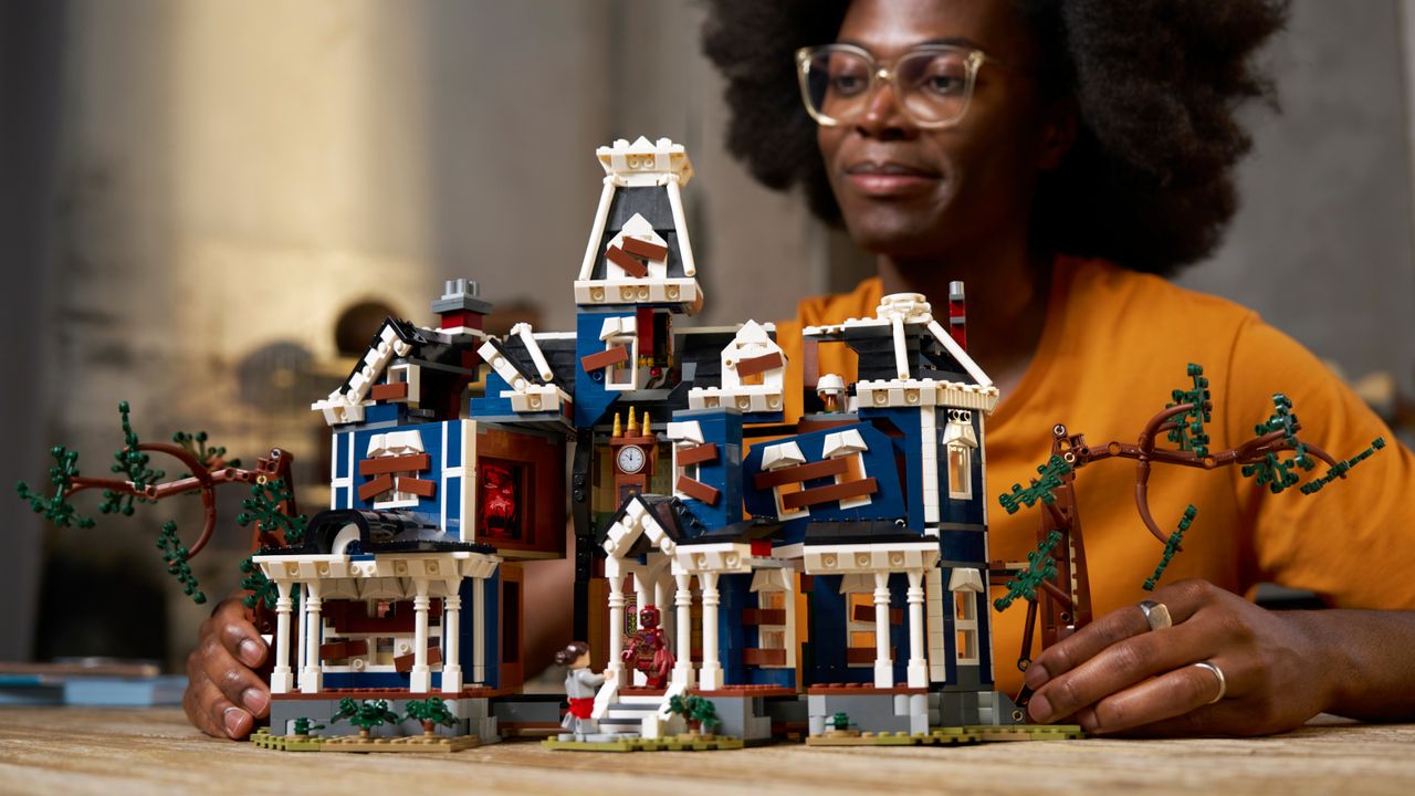 A woman looks down at the Lego Creel House while holding its sides