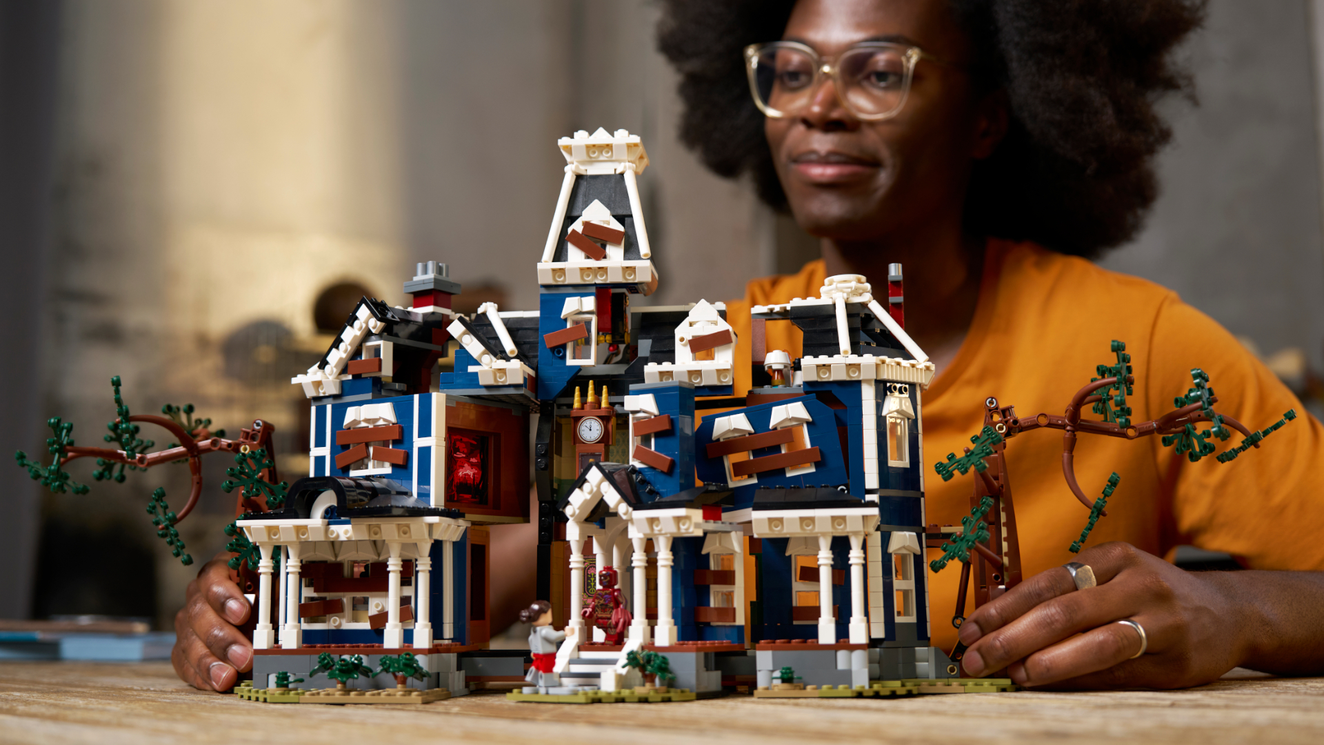 A woman looks down at the Lego Creel House while holding its sides