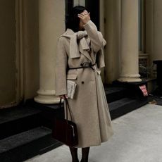 Woman wears beige coat, beige sweat and black tights. 