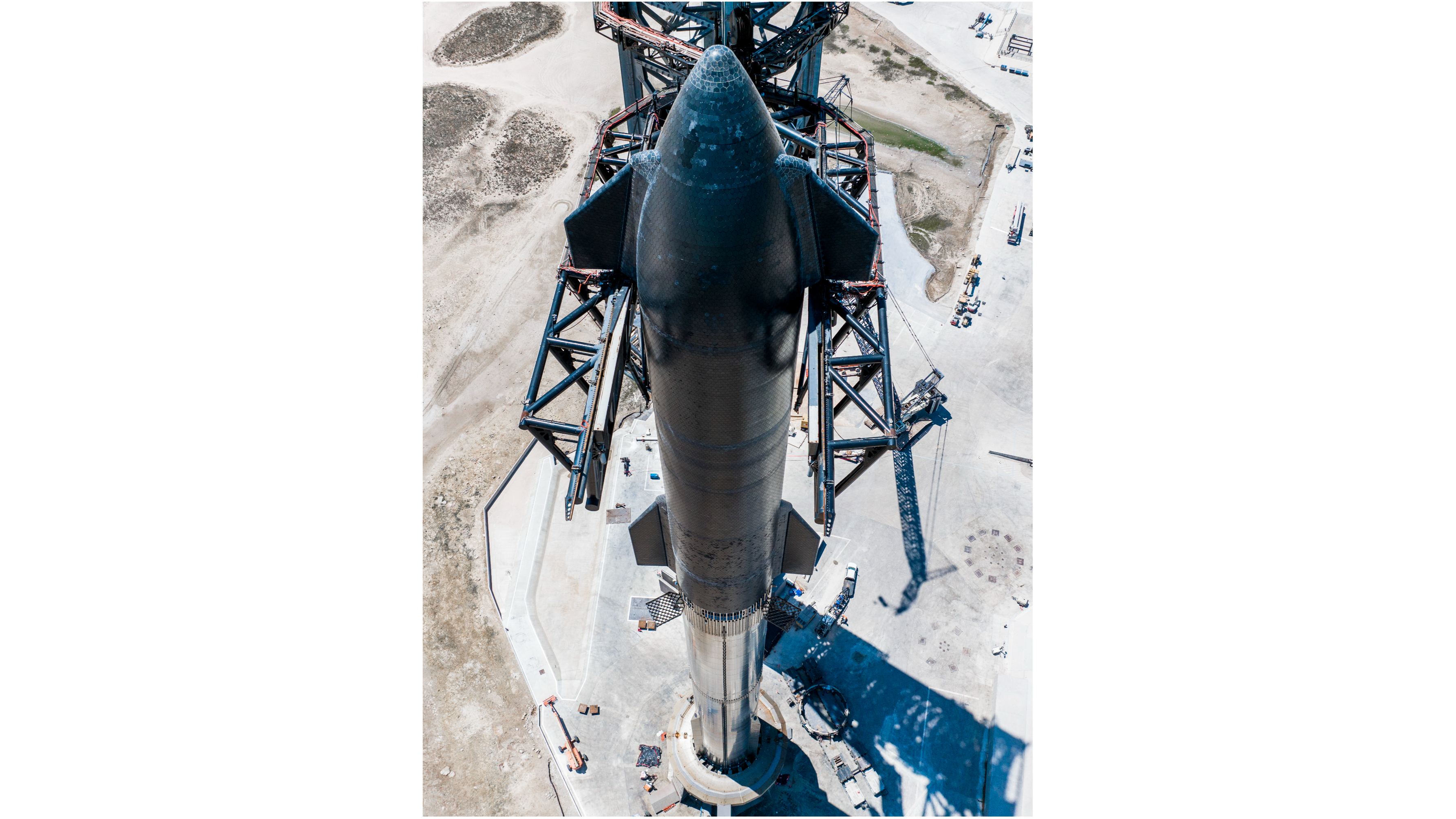 vista de cima do enorme veículo estelar da SpaceX na plataforma de lançamento, com uma paisagem de dunas ao fundo.