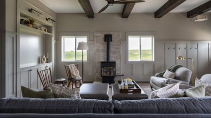a neutral yet moody barn living area with log burning stove, ceiling beams and comfortable furniture